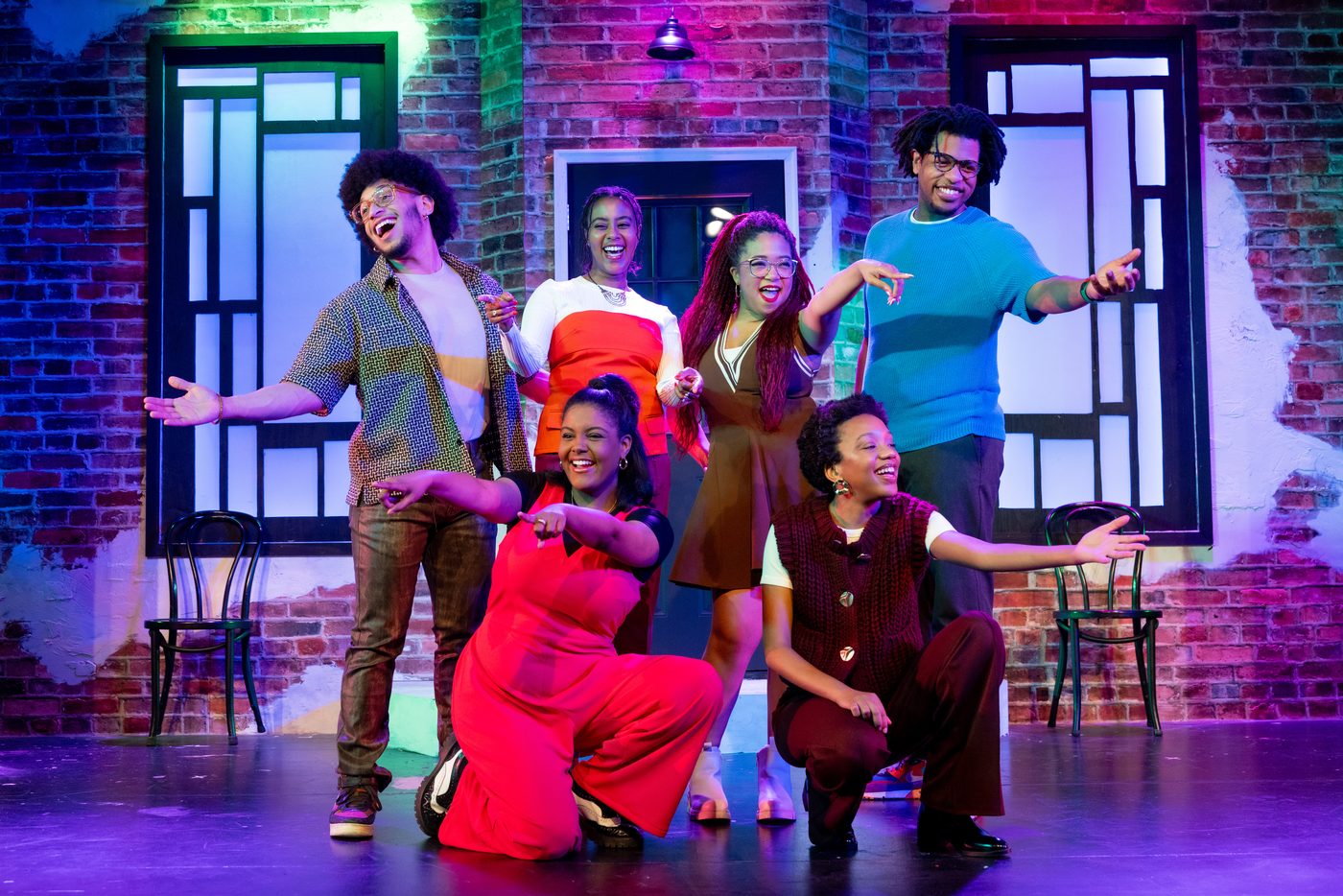 The cast of a Second City revue striking a group pose on a brick-walled stage set